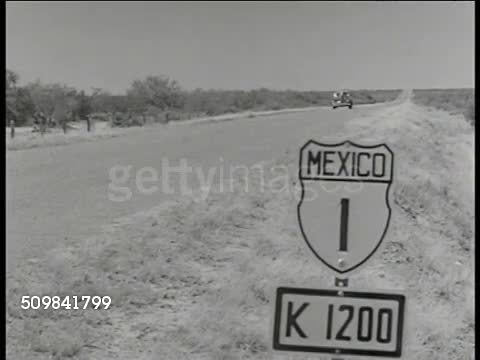 1946: MEXICO & FAMILY: WS Desert, plain, mountains BG. WS Car on highway, sign FG. WS Mexican family thumbing for ride, hitchhiking. MS Family, car passing. Pan American highway, tourists, vacation